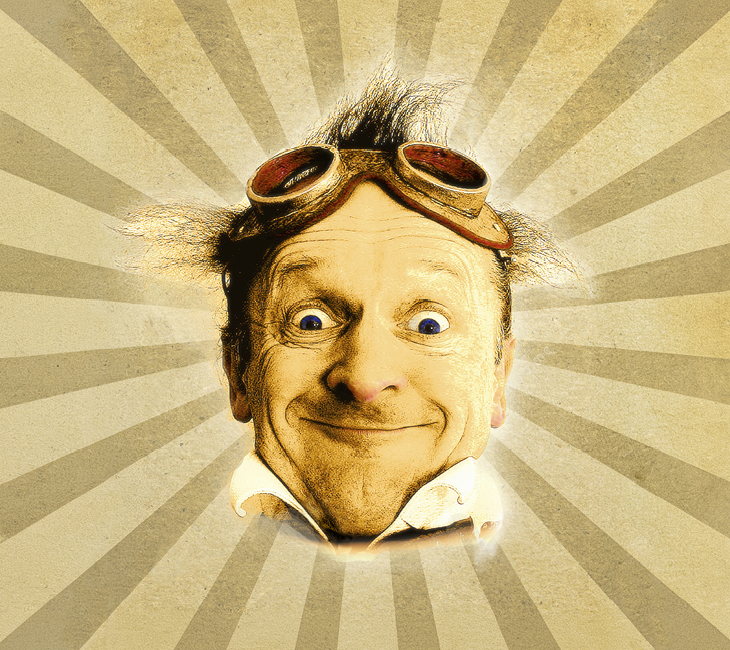 Man with messy hair and goggles on his head smiles widely in front of a vintage sunburst background.