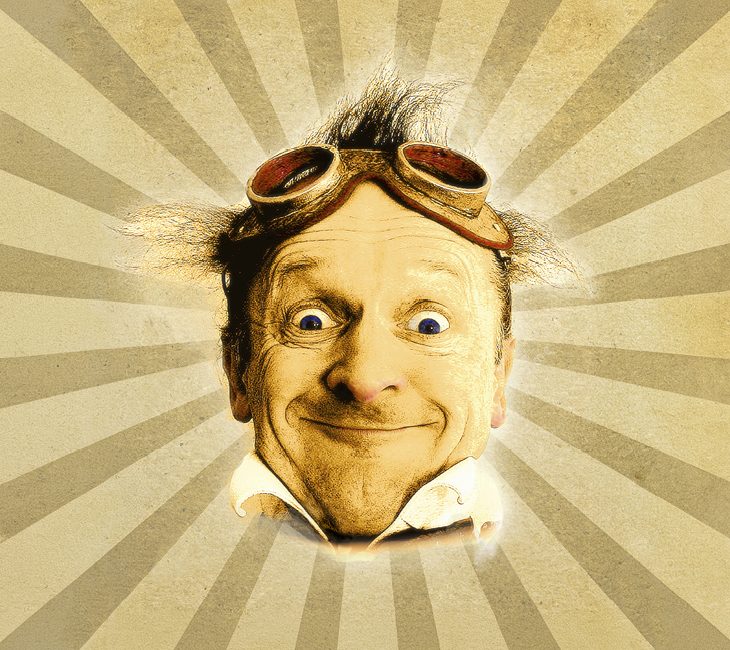Man with messy hair and goggles on his head smiles widely in front of a vintage sunburst background.