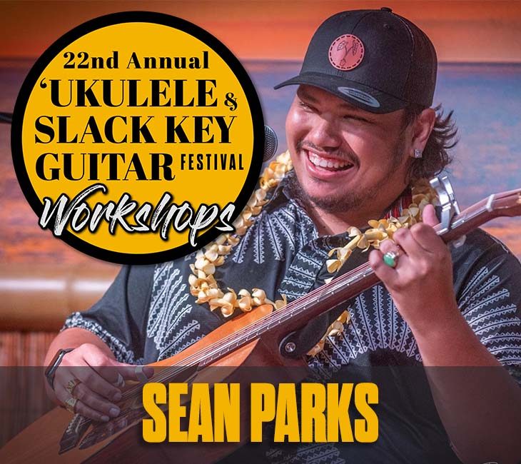 Musician playing guitar, wearing a floral lei and a hat, with a sign reading "22nd Annual 'Ukulele & Slack Key Guitar Festival Workshops" and the name "Sean Parks" displayed.